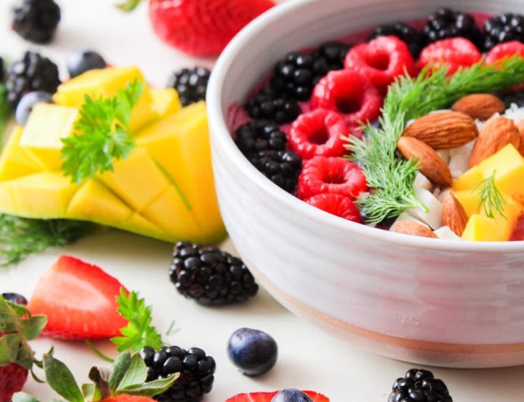 A vibrant bowl filled with fresh berries, mango, almonds, and herbs, perfect for a healthy snack or breakfast.